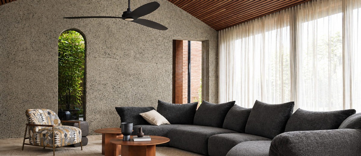 Black three-blade ceiling fan above a charcoal sectional sofa in a living room with sheer curtains and a timber ceiling