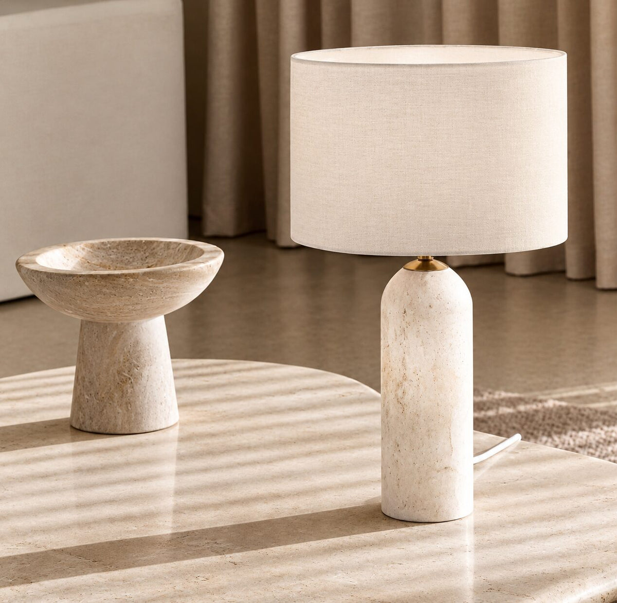 Table lamp with a white linen shade and a pale marble base on a stone coffee table