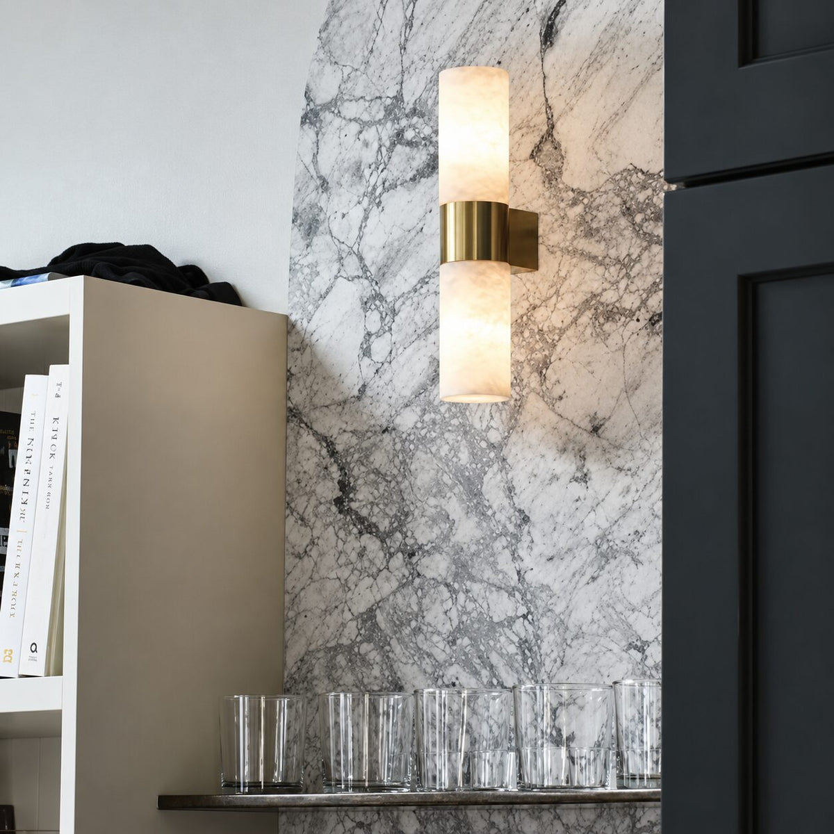 Alabaster and brass wall light mounted on a veined marble wall beside a bookshelf