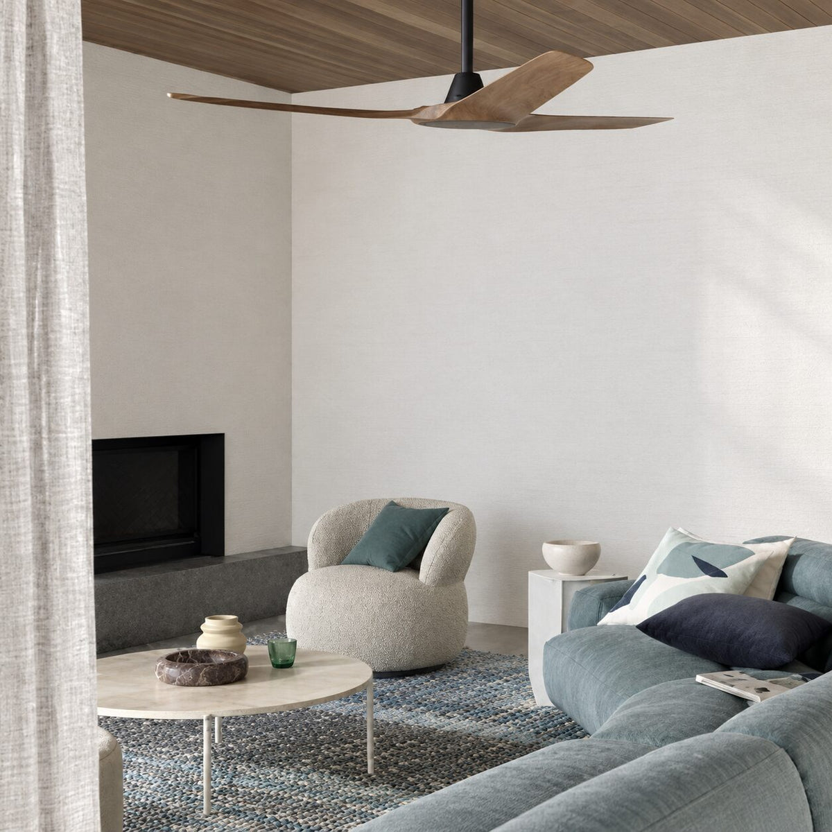 Minimal living room with a timber ceiling fan, a round boucle chair and a blue-grey sofa