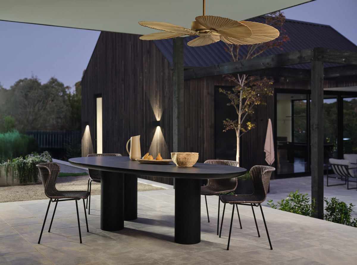 Palm-leaf style ceiling fan above an outdoor dining table and black chairs at dusk