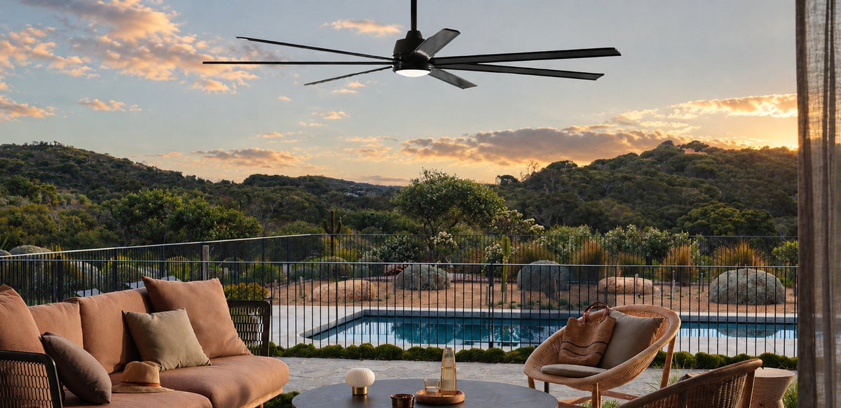 Black ceiling fan over an outdoor lounge with rattan chairs and a pool, looking across hills at sunset