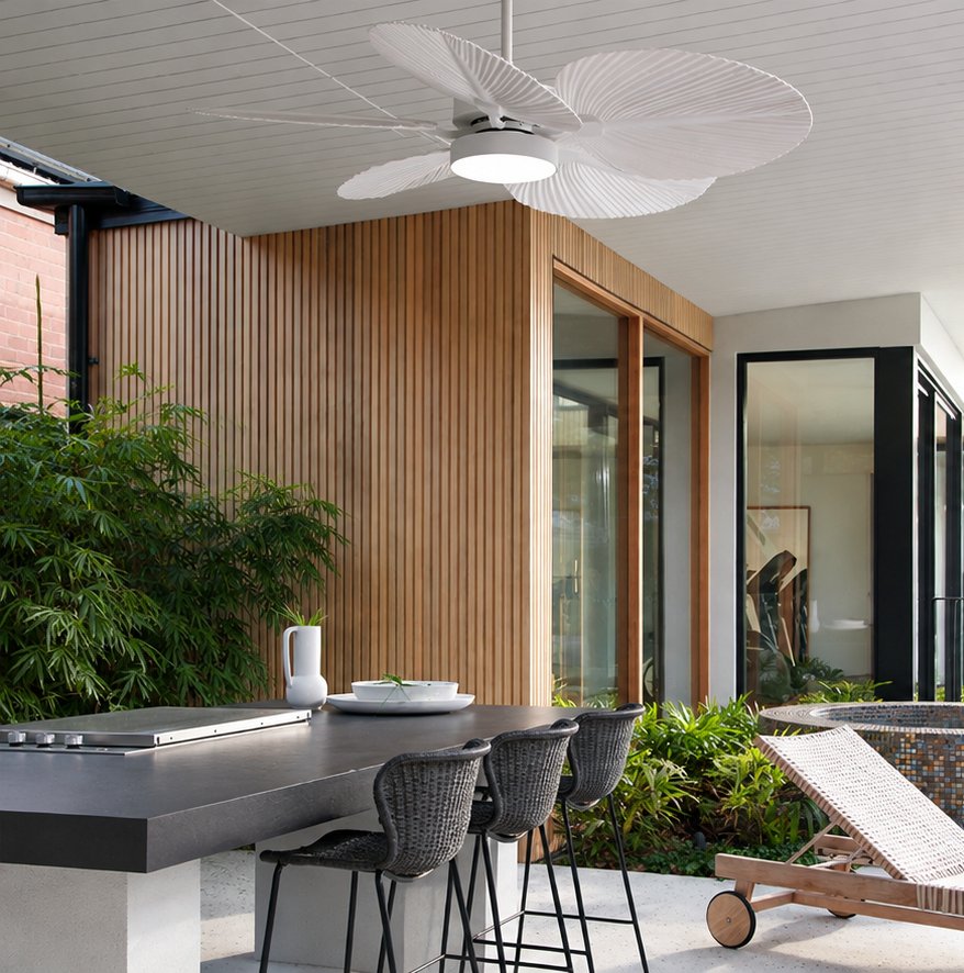 White ceiling fan with palm-leaf shaped blades above an outdoor kitchen bar with woven stools and a timber-clad wall