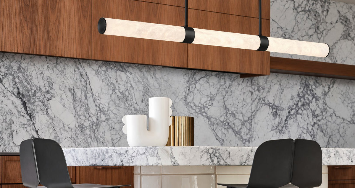 Long alabaster and black linear pendant light above a marble dining table with black chairs and timber cabinetry