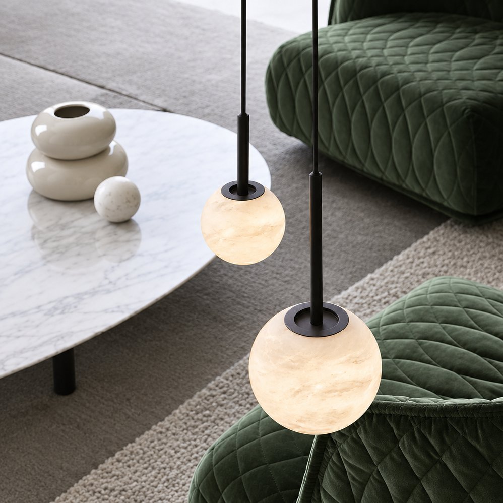 Two alabaster globe pendant lights on black stems hanging above a marble coffee table and green velvet armchairs